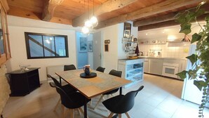Un comedor con mesa y sillas de madera, una cocina al fondo y una planta a la derecha.