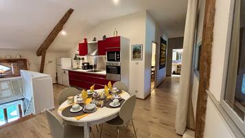 Una cocina moderna con armarios rojos, un comedor con una mesa preparada para dos personas, y vista al área de estar a través de una puerta abierta.