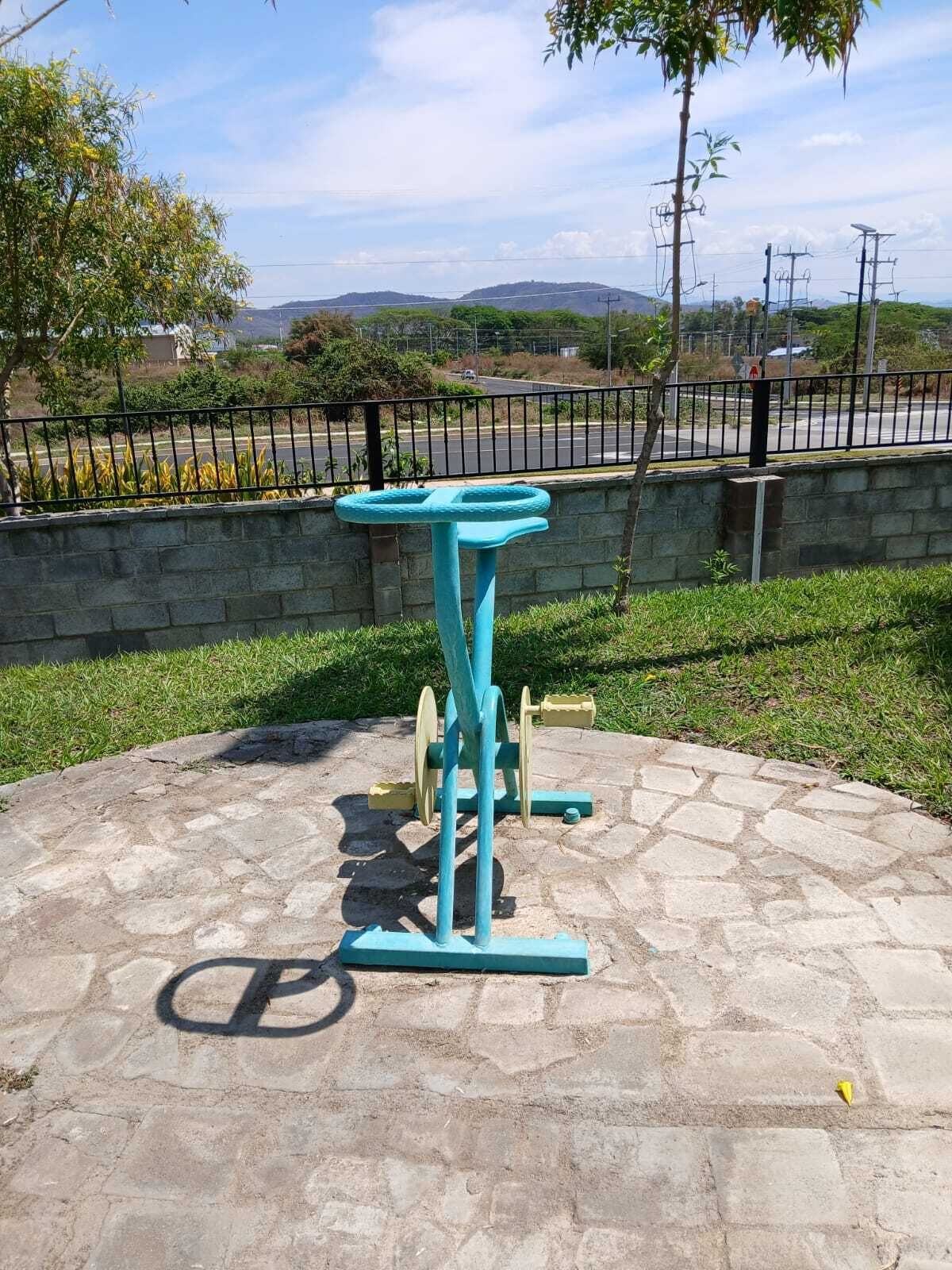 Una estación de ejercicio al aire libre en azul, con zona pavimentada de piedra, rodeada por una valla y follaje.