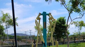 Un parque con equipo de ejercicio al aire libre, una zona pavimentada y una cerca al fondo.