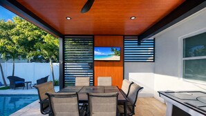 Un espace repas extérieur moderne, doté d’une piscine, d’un téléviseur fixé au mur et offrant une vue sur l’extérieur.