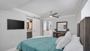 Une chambre à coucher avec un lit, un ventilateur de plafond, un téléviseur fixé au mur et une commode.