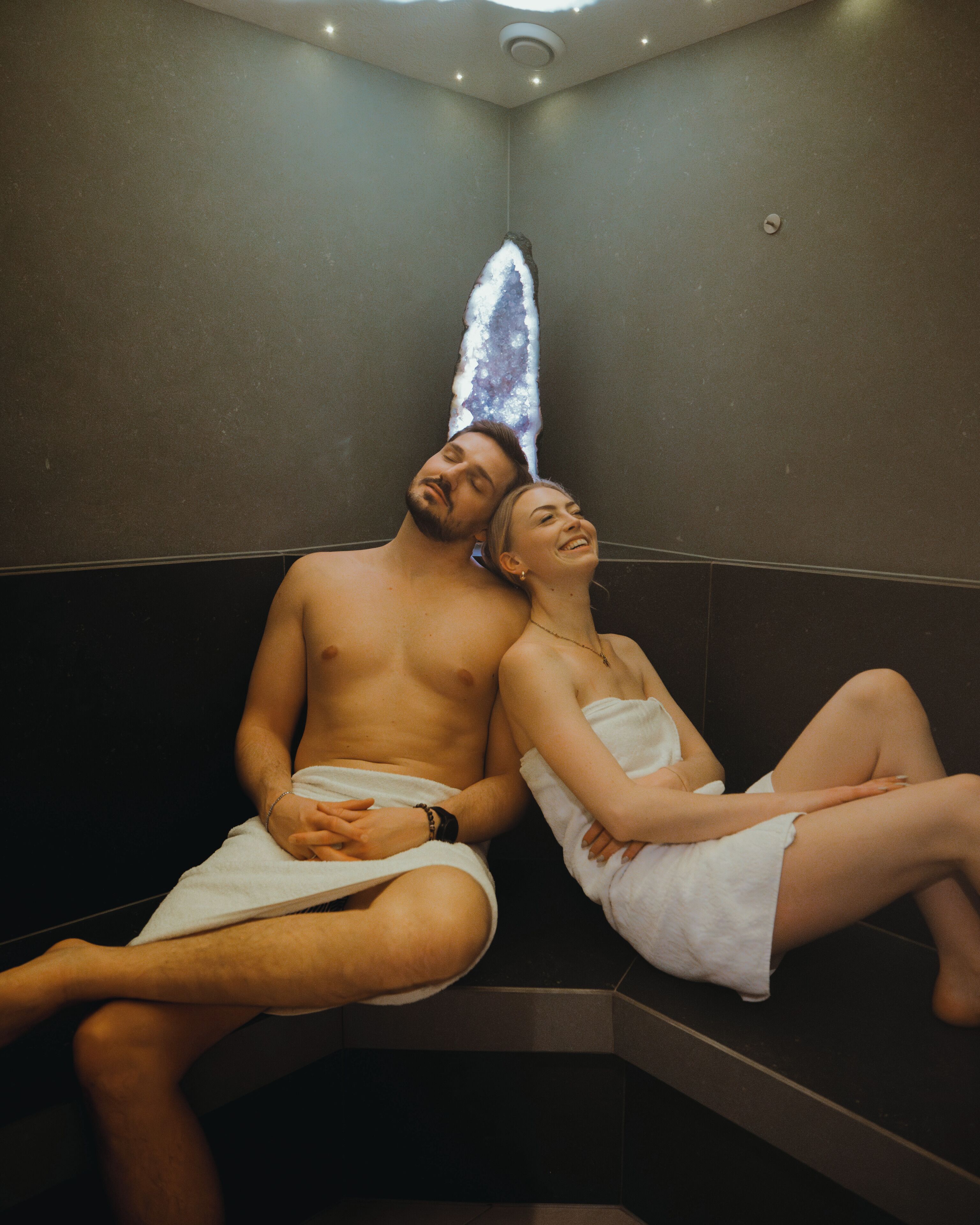 A couple sitting in a dimly lit room with a textured wall and a ceiling light fixture.
