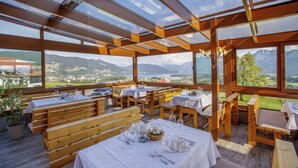 Un espacio de comedor al aire libre con bancos y mesas de madera, amplios ventanales con vistas a las montañas.