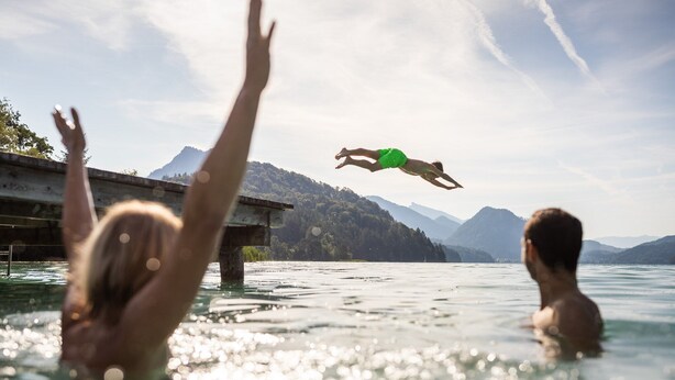 Una persona se sumerge en un cuerpo de agua, con montañas al fondo.