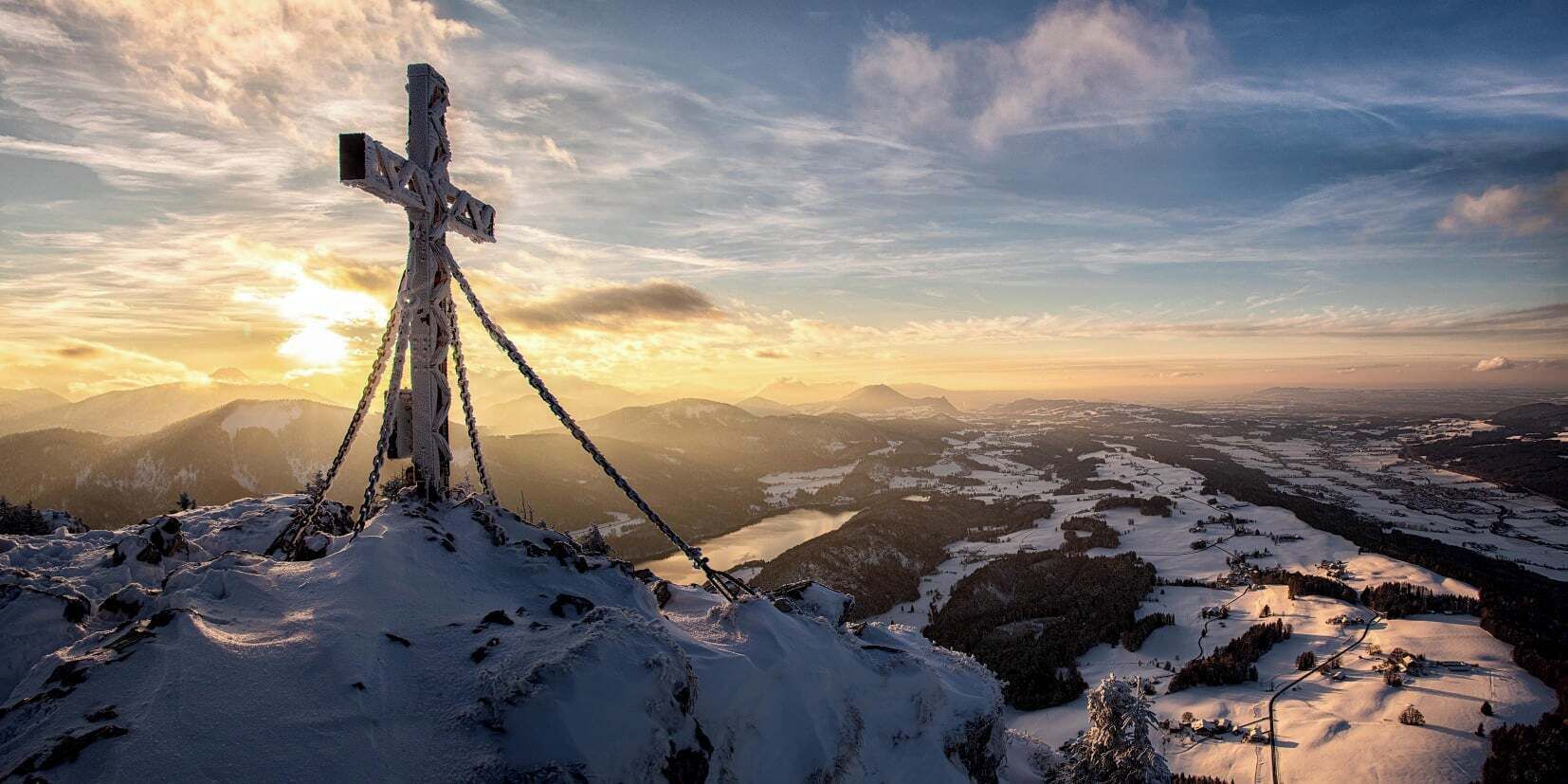 A snow-covered mountain peak with a cross at the summit and a chain attached to it.