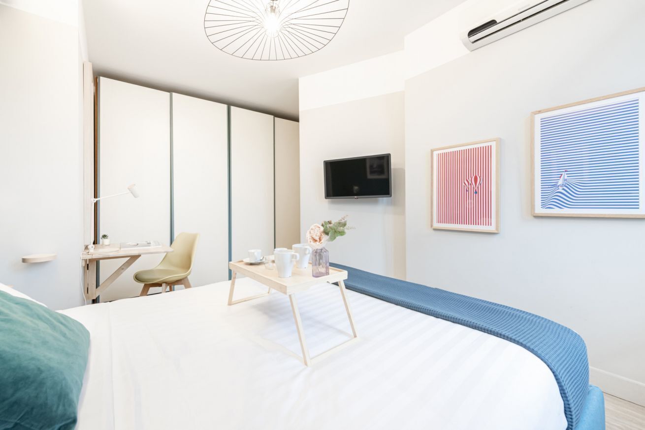 A modern hotel room with a bed, a desk, a chair, and a TV.