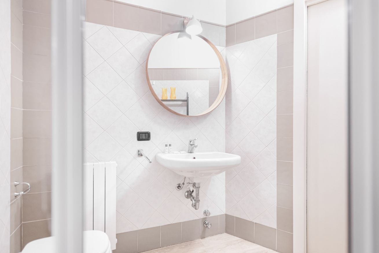 A modern bathroom with a round mirror, white sink, and beige tiles.