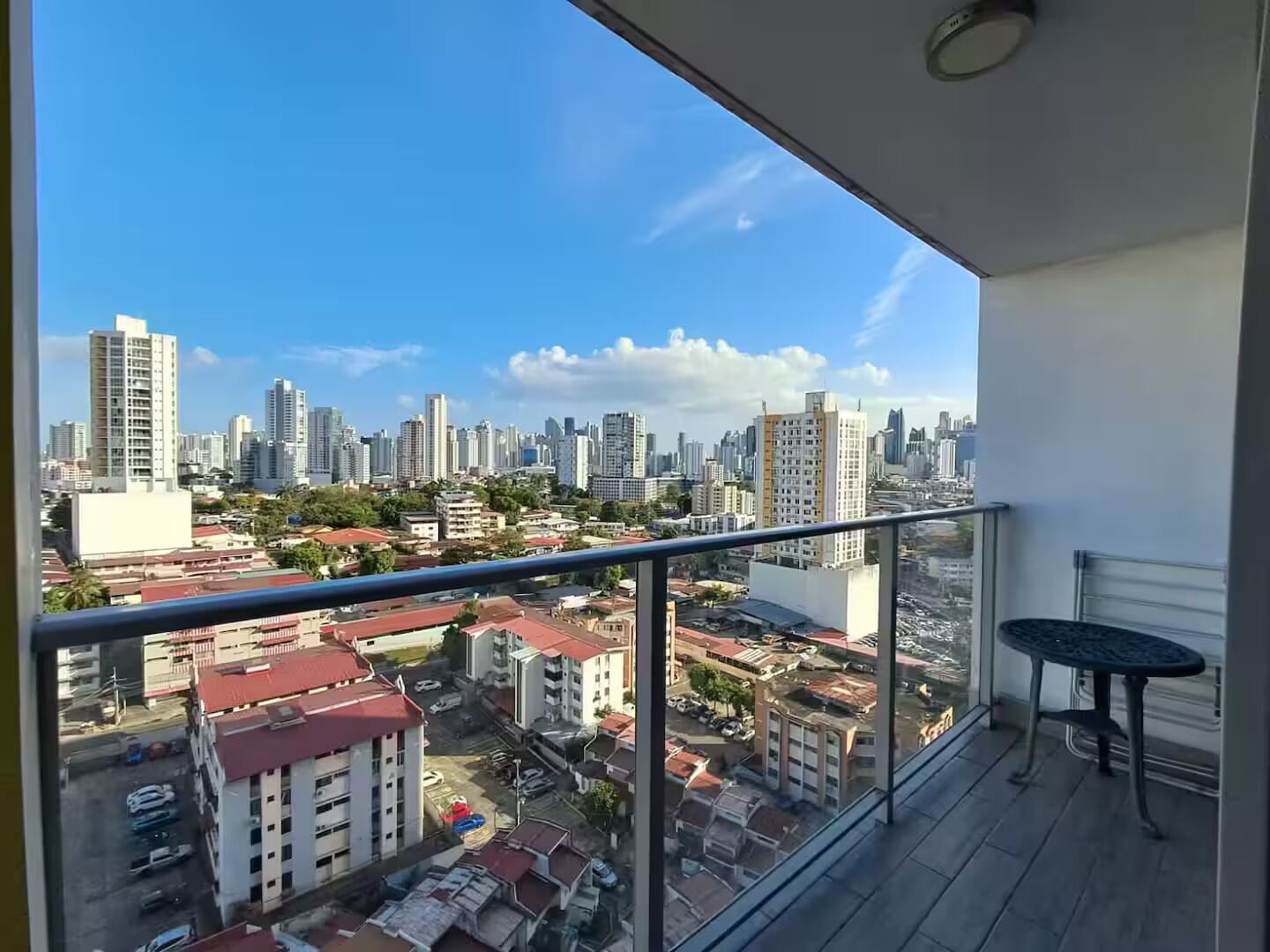 Un balcon offrant une vue dégagée sur le paysage urbain, avec notamment des immeubles de grande hauteur et un parking.