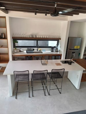 A modern kitchen with a large island, black wire chairs, a coffee machine, and a refrigerator. - 5 min to Cocles Beach | Modern, Quiet Home with A/C • Walk to Shops (Coclea)