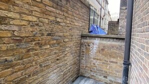 Un callejón estrecho con paredes de ladrillo, un toldo azul en una ventana y una tubería negra a la derecha.
