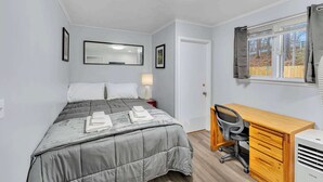 A bedroom with a bed, a desk, a chair, a lamp, a mirror, and a window with curtains. - Main Lineup Apt 4 - All Star Baseball Rentals (Oneonta)