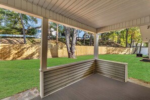 A covered outdoor seating area with a wooden deck and a view of a well-maintained lawn and trees. - Main Lineup Apt 4 - All Star Baseball Rentals (Oneonta)