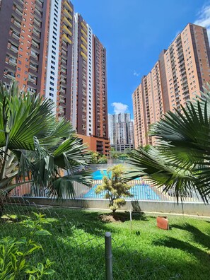 A residential area with high-rise apartment buildings, a fenced pool, and lush greenery. - Beautifully furnished apartment in a secure complex   (Medellín)