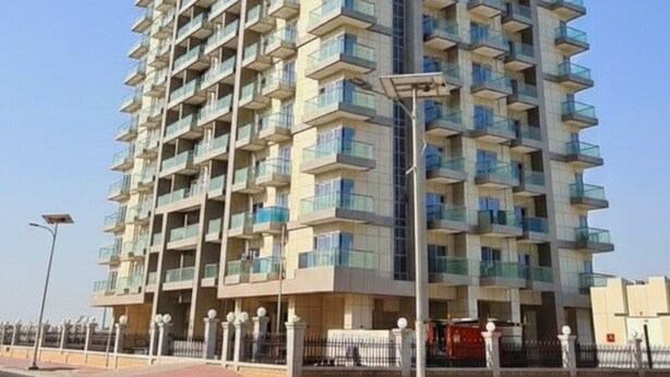 A high-rise residential building with multiple balconies, a clear sky, and a street in the foreground. - Modern Studio with Balcony in Dubai Sports City (Dubai)