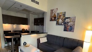 A modern living room with a grey sofa, a white coffee table, and a kitchen in the background. - Modern Studio with Balcony in Dubai Sports City (Dubai)