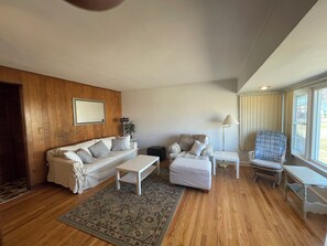 Ein Wohnzimmer mit Holzpaneelen, einem weißen Sofa, einem gemusterten Teppich und einem Fenster mit Vorhängen.