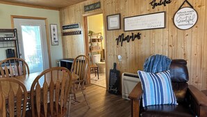 A cozy cabin interior with wooden walls, a dining area with wooden chairs, a leather sofa, and various framed signs with messages. - Perfect 3-bedroom cabin with AC in pleasant Moravia (Moravia)