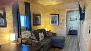 A cozy cabin interior with a wooden floor, a sofa with patterned cushions, a dining table with chairs, and framed pictures on the walls. - Perfect 3-bedroom cabin with AC in pleasant Moravia (Moravia)