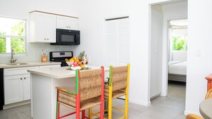 A modern kitchen with white cabinets, a black microwave, and a dining area with colorful chairs. - Charming 3bdrm villa w/ panoramic ocean views, pool & patio, 5 min walk to beach (Providenciales)