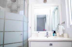 Ein modernes Badezimmer mit Duschkabine aus Glas, einem weißen Waschtisch mit Spiegel und Pflegeprodukten.