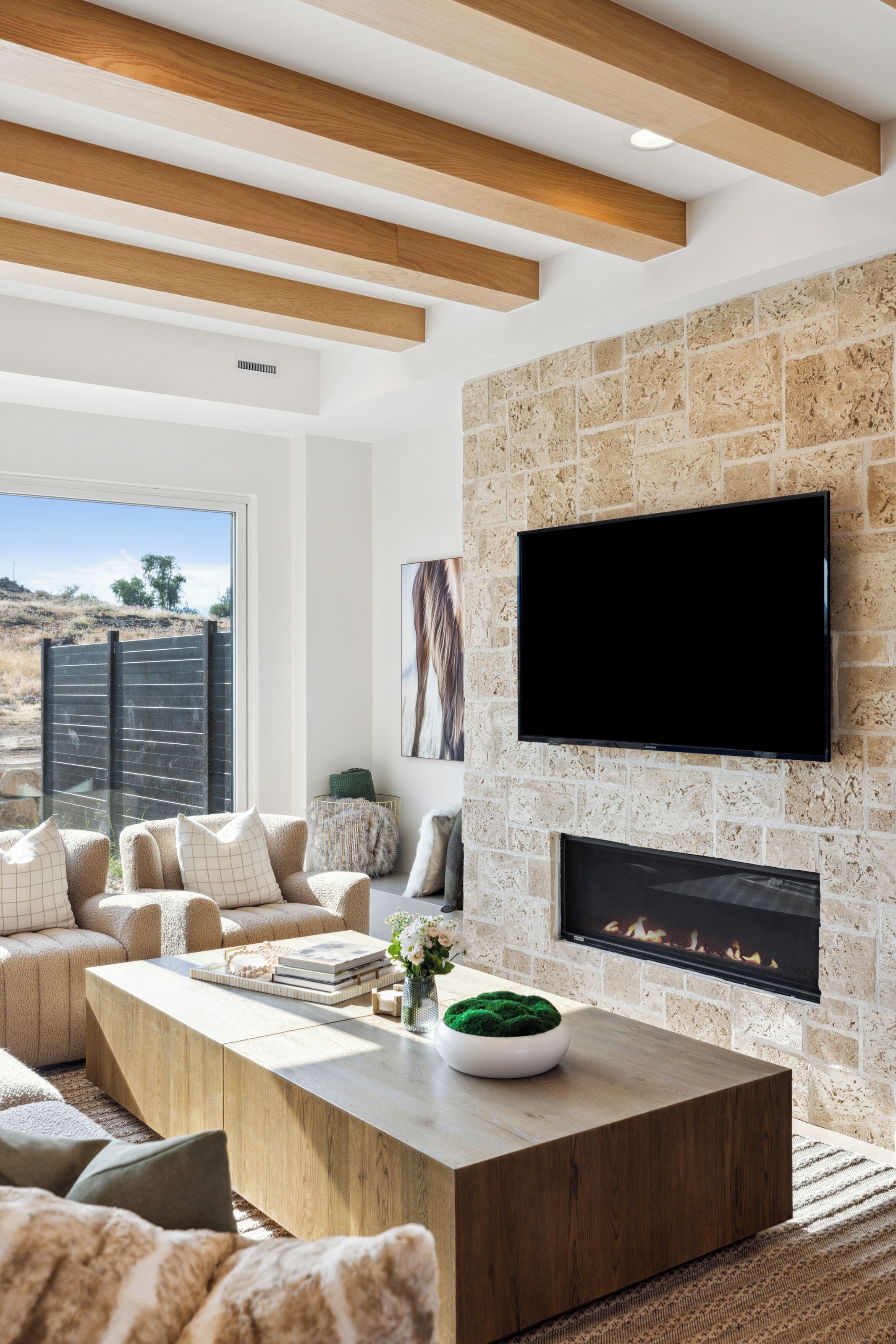 Una sala de estar moderna con chimenea de piedra, un televisor de pantalla plana y un amplio ventanal con vistas al paisaje.