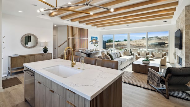 Una cocina moderna con una isla grande, vigas de techo de madera y un comedor con vistas al exterior.