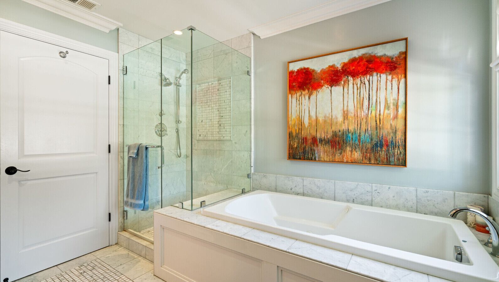 A modern bathroom with a glass-enclosed shower, a large bathtub, and a wall-mounted painting.