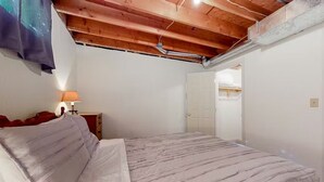 Een slaapkamer met een bed, nachtkastje, lamp en een houten plafond.