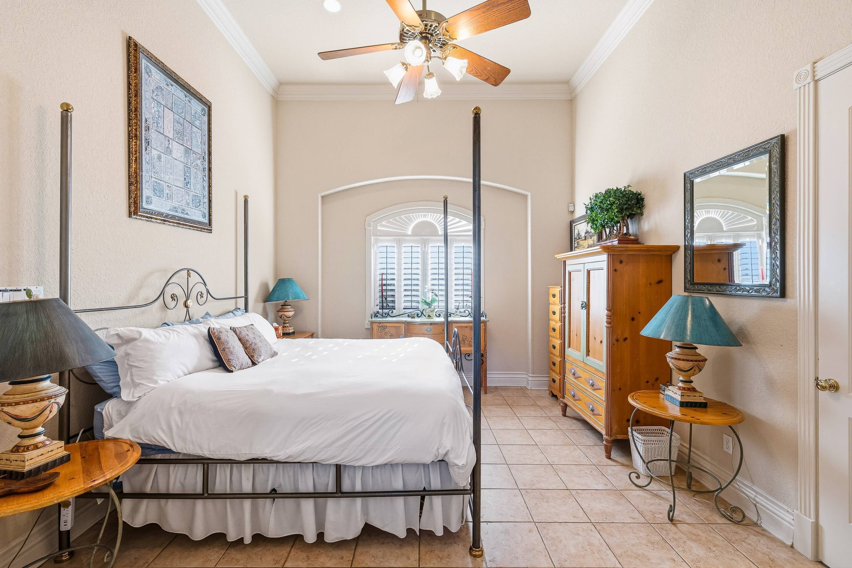 Un dormitorio con cama, ventilador de techo, cómoda, espejo y ventana con vistas.