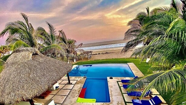 A swimming pool with a thatched roof, palm trees, and a view of the beach. - Casa Del Carmen (Santa María Colotepec)