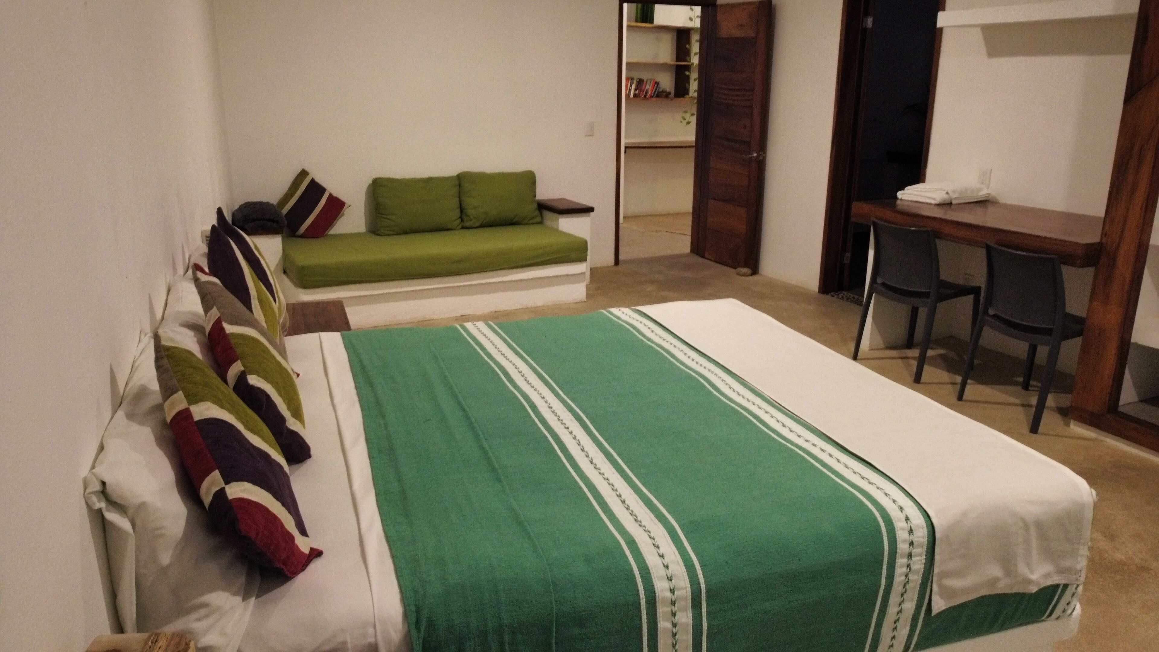 Um quarto com cama, sofá verde, escrivaninha e cadeira.