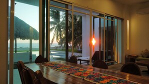 A dining area with a view of the ocean and palm trees, featuring a wooden table and chairs. - Casa Del Carmen (Santa María Colotepec)