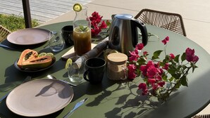 Et bord dækket udendørs med iste, en frugt i hjerteform, en kop, en elkedel og en blomsterdekoration.