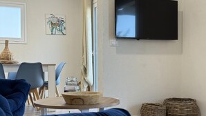 Ein modernes Wohnzimmer mit einem blauen Sofa, einem runden Holztisch mit einer Schüssel, einem an der Wand befestigten Fernseher und Korbwannen auf dem Boden.