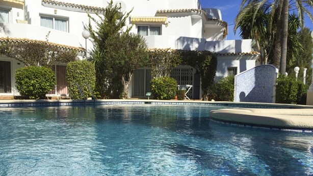 A swimming pool with clear blue water, surrounded by a white building with balconies and palm trees. - 06 Ap2116 in Denia With 2 Bedrooms and 1 Bathrooms (Denia)