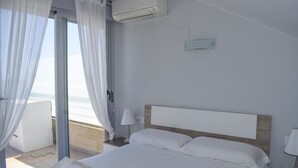 Ein Hotelzimmer mit Bett, Nachttisch, Lampe, Klimaanlage und Meerblick durch eine Glastür.
