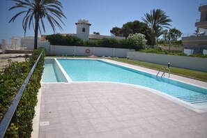 A rectangular swimming pool with a tiled deck, surrounded by a low hedge and palm trees. - 03 At1102 in Denia With 1 Bedrooms and 2 Bathrooms (Denia)