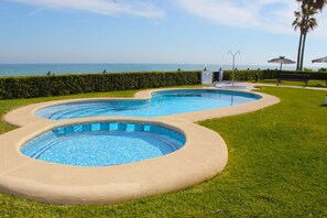 A swimming pool with a curved design, surrounded by well-maintained grass and a hedge. - 01 At2201 in Denia With 2 Bedrooms and 2 Bathrooms (Denia)