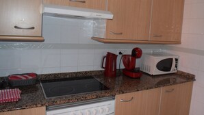 A kitchen with wooden cabinets, a stove, a microwave, and a red kettle. - Ap3212 in Denia With 3 Bedrooms and 2 Bathrooms (Denia)