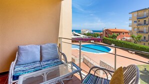 Ein Balkon mit Glastisch und Stühlen mit Blick auf einen Swimmingpool und einen Strand.