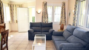 Ein Wohnzimmer mit grauem Sofa, einem Glastisch und blumigen Vorhängen.