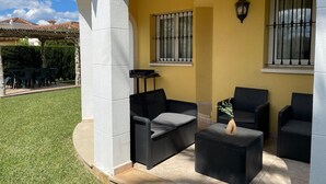 Eine Terrasse mit Gartenmöbeln, darunter eine Couch und Stühle, ein kleiner Tisch und ein Blumentopf.