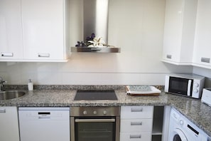 A modern kitchen with white cabinets, a granite countertop, a built-in oven, a dishwasher, a microwave, and a stainless steel range hood. - Ap2216 in Denia With 2 Bedrooms and 2 Bathrooms (Denia)