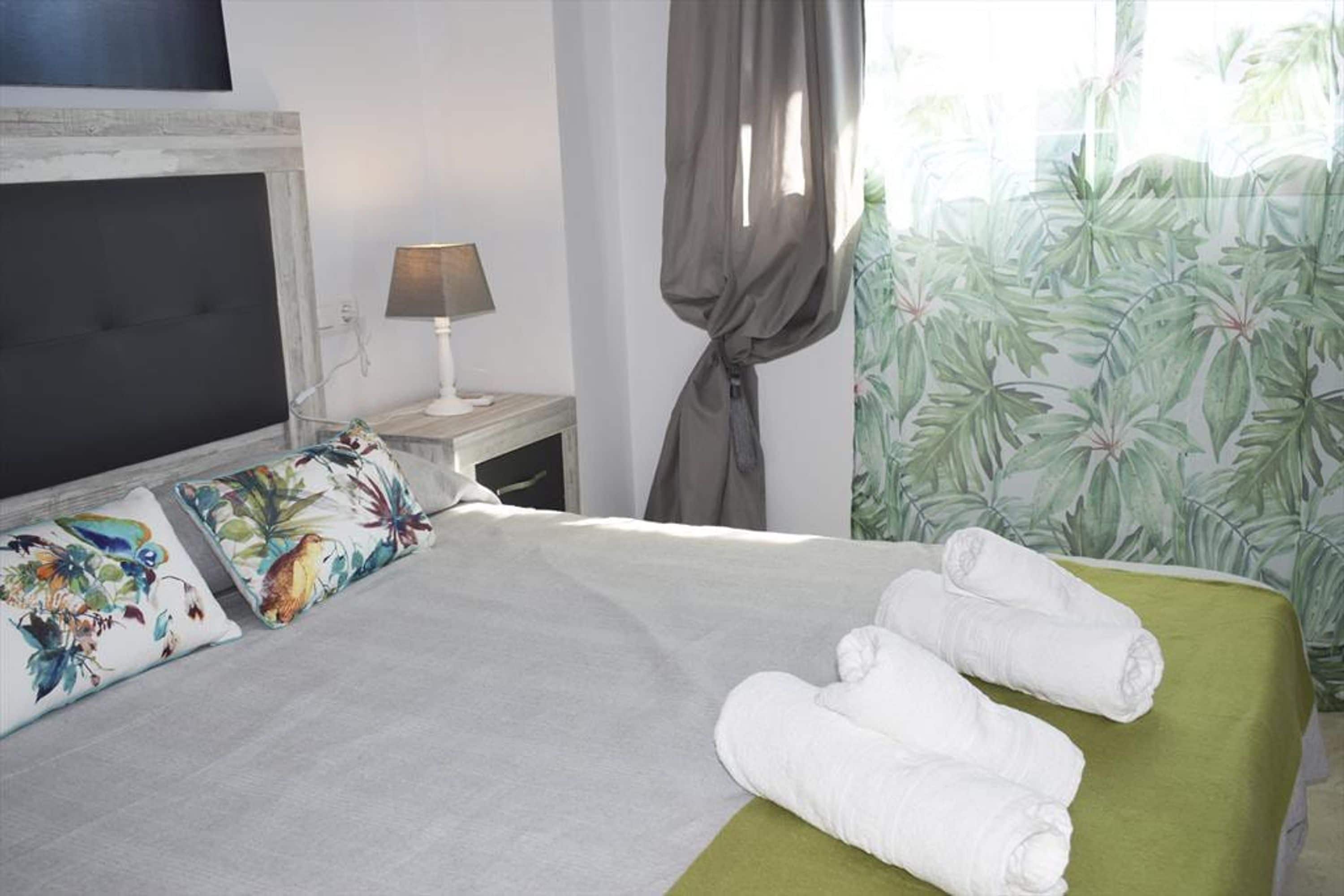 Una cama bien hecha con una colcha verde y dos almohadas con estampado tropical.