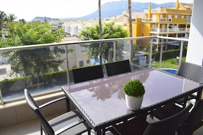 A balcony with a glass table and chairs, a potted plant, and a view of buildings and greenery. - Ap2216 in Denia With 2 Bedrooms and 2 Bathrooms (Denia)
