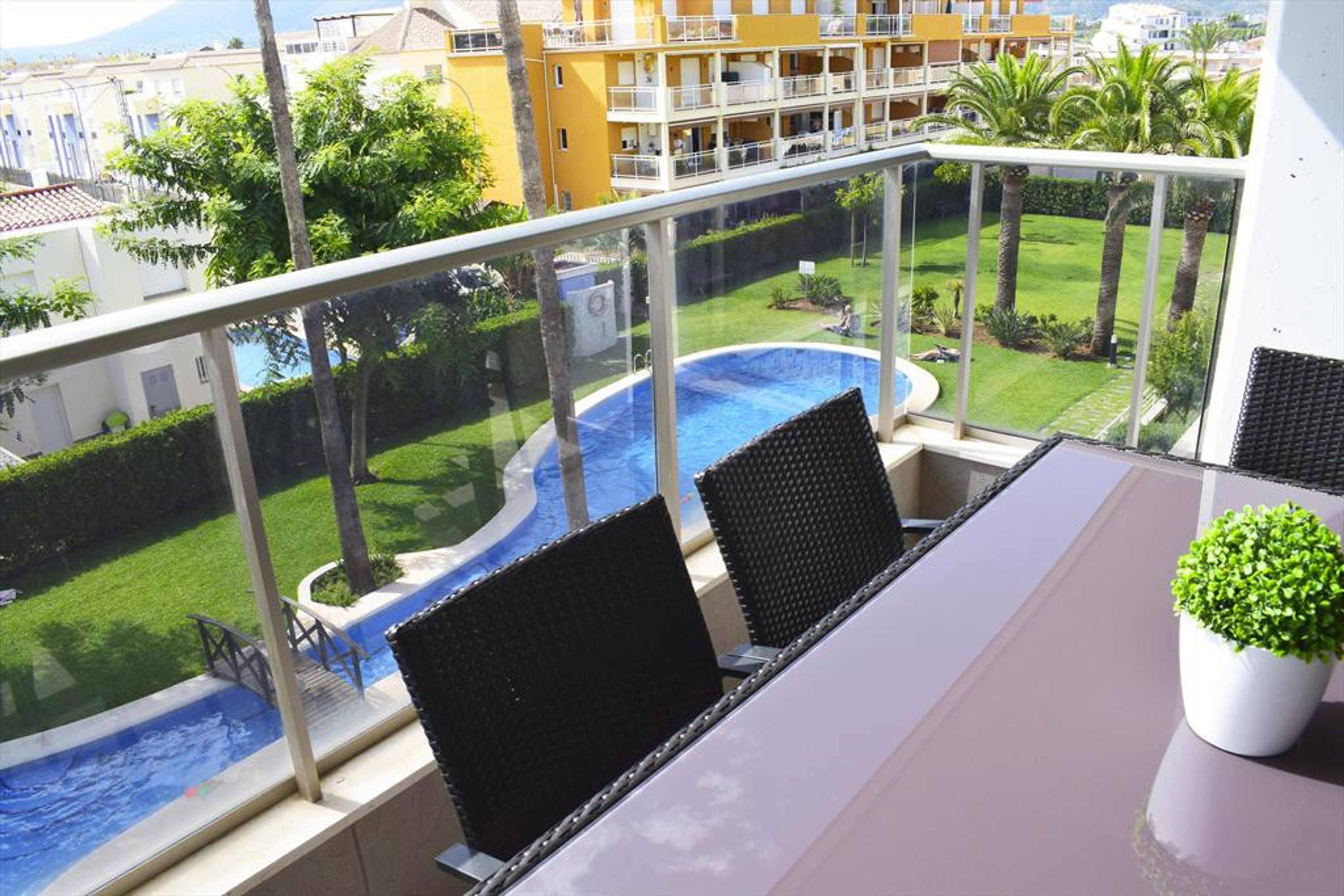 Un balcon donnant sur une piscine, une pelouse et un bâtiment jaune en arrière-plan.