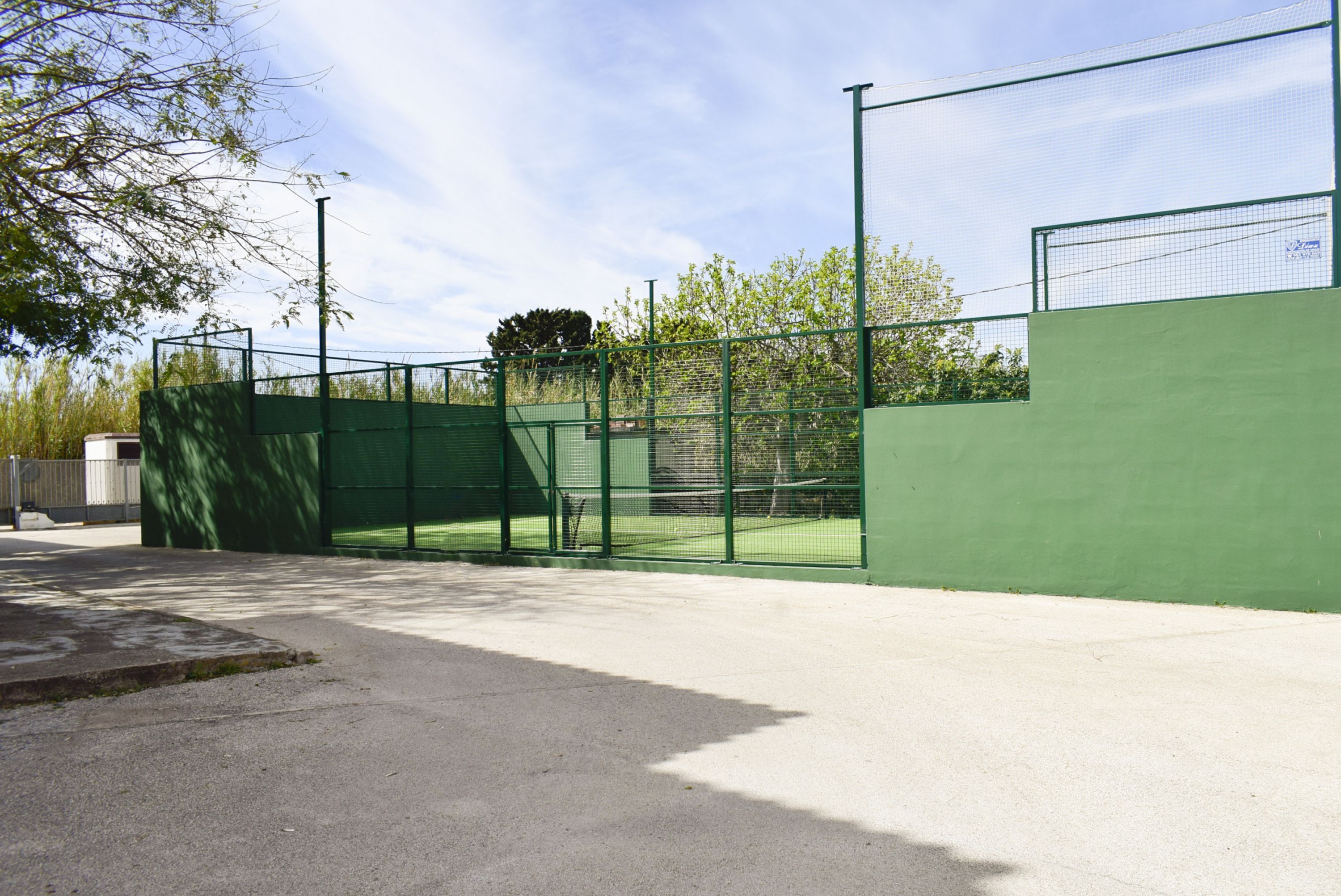 An outdoor tennis court with a green fence and a concrete surface.