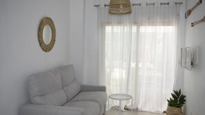 Ein minimalistisches Wohnzimmer mit grauem Sofa, einem kleinen runden Tisch, einer Korbtasche-Lampe und transparenten Vorhängen.