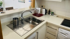 Una cocina moderna con un lavamanos de acero inoxidable, un hervidor, una cafetera y un lavavajillas.